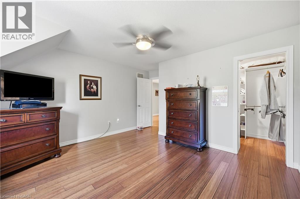 Spacious room featuring wood-finish flooring, a contemporary ceiling fan with integrated lighting, a bright white door, and an open closet with built-in shelving - 10 Kopperfield Lane, Hamilton, ON - Indoor