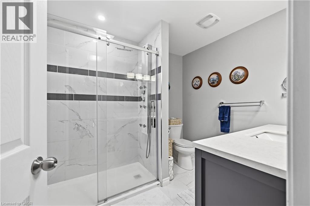 Glass-enclosed shower with a multi-function shower system and white marble-look tile surround featuring dark accent bands - 10 Kopperfield Lane, Hamilton, ON - Indoor Photo Showing Bathroom