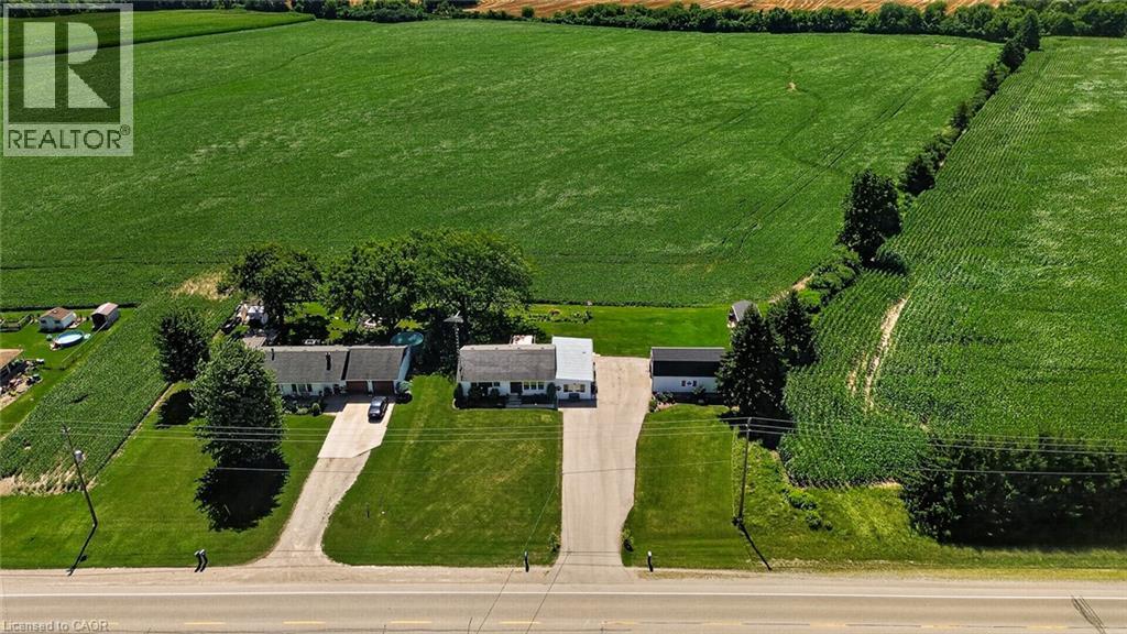 Expansive agricultural fields surround a property featuring a white residence with an attached garage, a separate outbuilding, and a gravel driveway - 184726 Cornell Road, Tillsonburg, ON - Outdoor