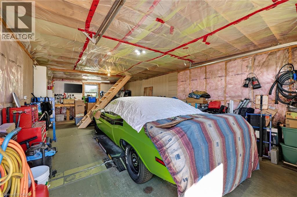 Expansive garage space featuring exposed wood framing, ceiling insulation, and a built-in wooden staircase - 184726 Cornell Road, Tillsonburg, ON - Indoor