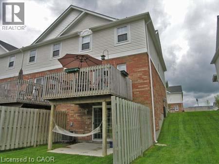 Rear exterior featuring a brick and siding facade, a raised wood deck, and a lower-level patio with a sliding glass door - 151 Clairfields Drive E Unit# 39, Guelph, ON - Outdoor With Exterior