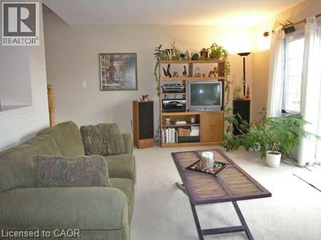 Bright living space featuring light-colored carpeting, neutral wall tones, and a large window with vertical blinds - 151 Clairfields Drive E Unit# 39, Guelph, ON - Indoor Photo Showing Living Room
