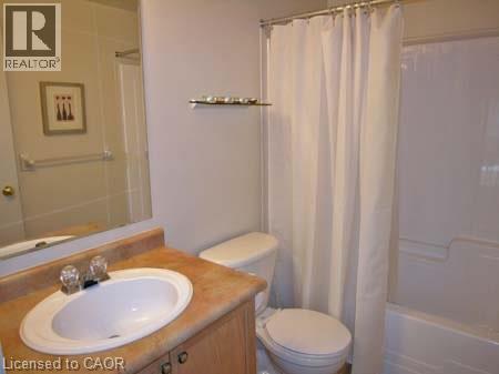 Bathroom featuring a wood-finish vanity with an oval basin sink, a light-toned countertop, a full-width wall mirror, and a white bathtub with an integrated shower - 151 Clairfields Drive E Unit# 39, Guelph, ON - Indoor Photo Showing Bathroom