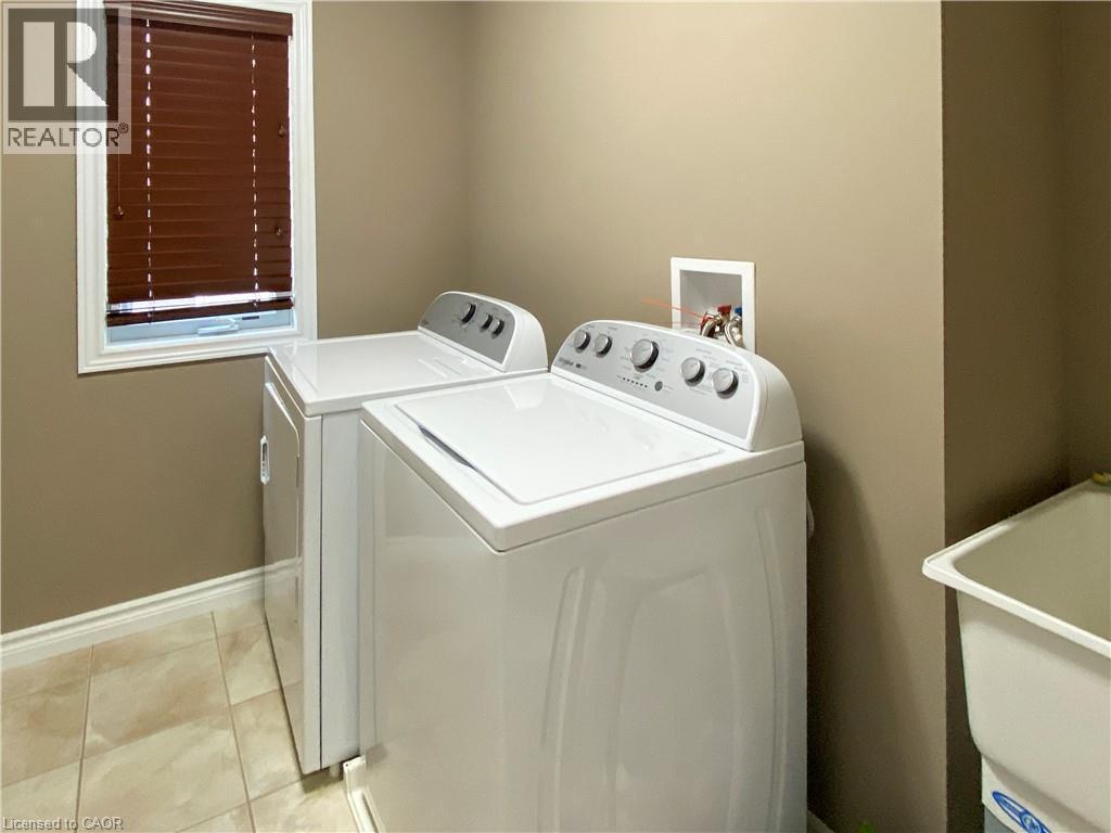 Laundry area featuring a top-load washer, a front-load dryer, a utility sink, and tile flooring - 180 Huck Crescent, Kitchener, ON - Indoor Photo Showing Laundry Room