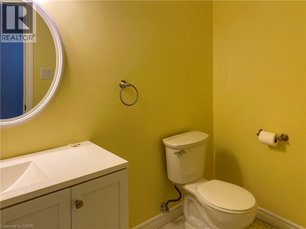 Bathroom featuring a white vanity with integrated sink, a circular mirror, and a standard toilet - 180 Huck Crescent, Kitchener, ON - Indoor Photo Showing Bathroom