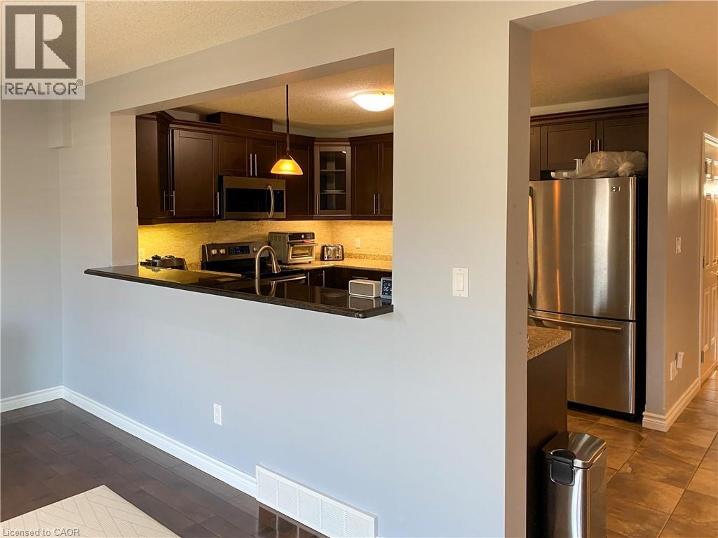 Kitchen featuring dark wood cabinetry, stainless steel appliances, black countertops, and under-cabinet lighting - 180 Huck Crescent, Kitchener, ON - Indoor Photo Showing Kitchen