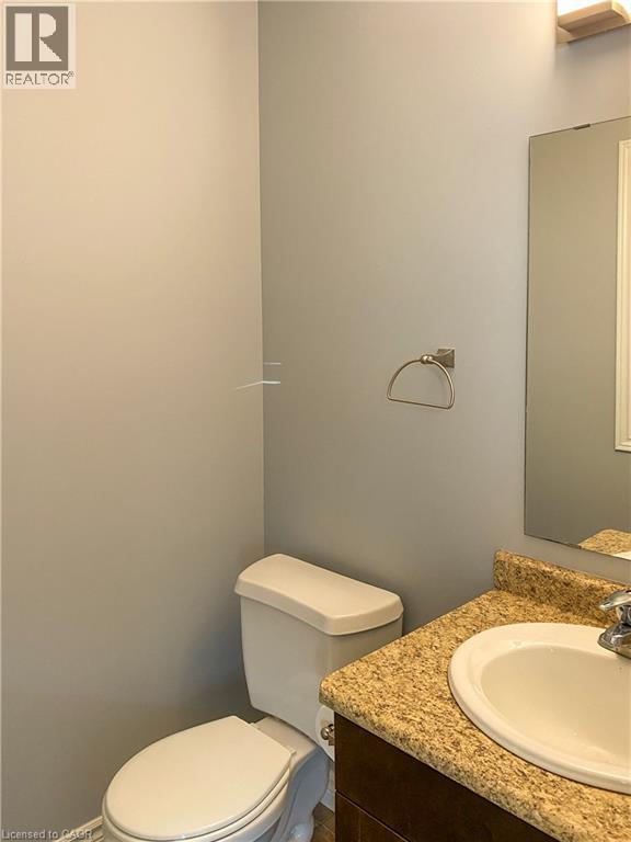 Powder room featuring a white toilet, dark wood-finish vanity with a granite-look countertop, and an undermount sink - 180 Huck Crescent, Kitchener, ON - Indoor Photo Showing Bathroom