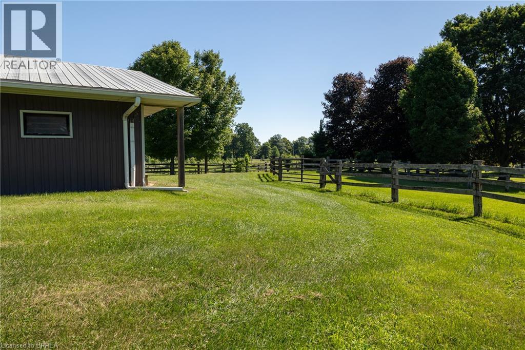 Expansive green lawn bordering a property structure with a metal roof and rain gutter system, featuring a fenced perimeter and mature trees - 269 Brant County Road 22, Ancaster, ON - Outdoor