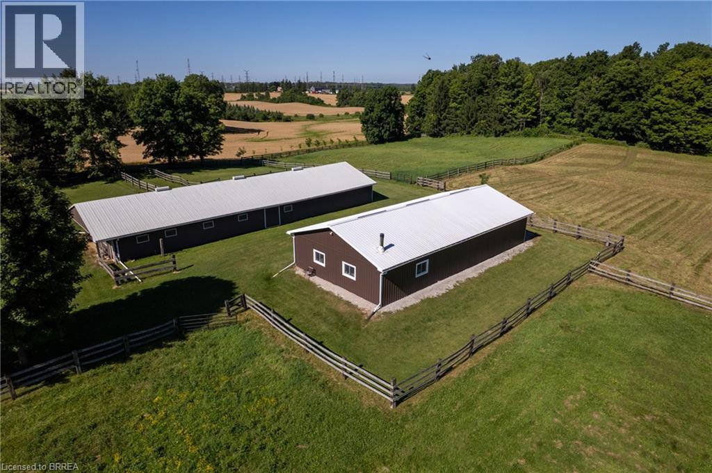 Two dark-toned outbuildings with metal roofs, surrounded by fenced green pastures - 269 Brant County Road 22, Ancaster, ON - Outdoor With View