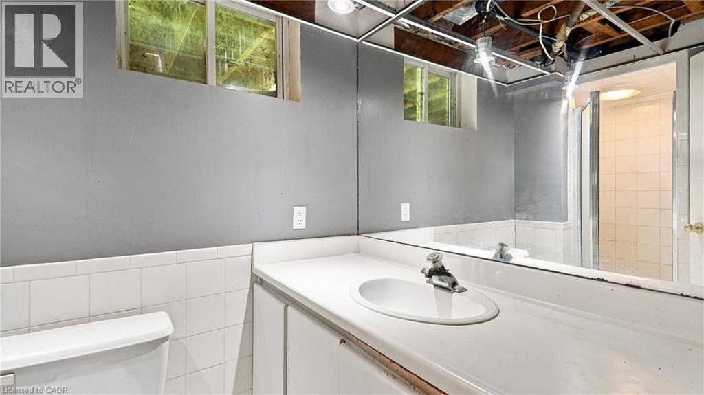 Bathroom featuring a spacious vanity with an integrated sink, large wall-mounted mirror, white ceramic wall tile, gray painted walls, and a shower with a glass enclosure - 524 Dorval Drive, Ancaster, ON - Indoor Photo Showing Bathroom