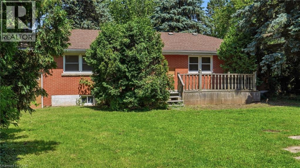 Brick exterior residence featuring a wood-tone deck with railing, a brown shingle roof, and multiple windows - 524 Dorval Drive, Ancaster, ON - Outdoor