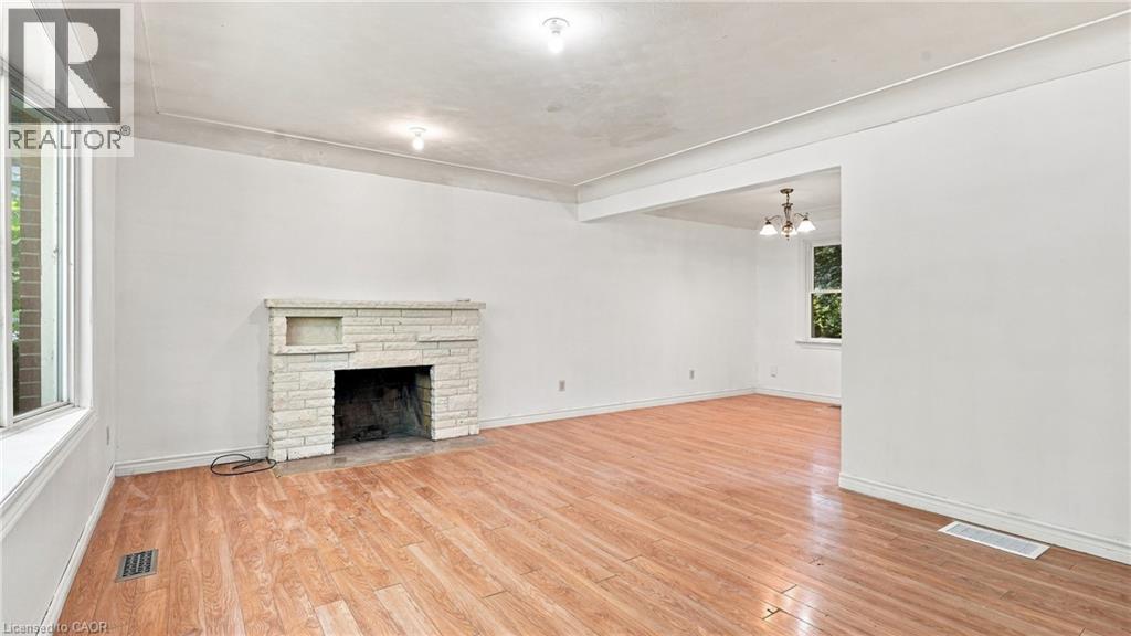 Spacious interior featuring wood-finish flooring, a stone-clad fireplace with mantel, and white walls - 524 Dorval Drive, Ancaster, ON - Indoor Photo Showing Other Room With Fireplace