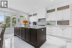 Expansive kitchen featuring a large central island, white cabinetry with gold-tone hardware, and polished marble-look flooring - 
