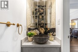 Powder room featuring a vessel sink on a light gray countertop, gold-toned wall-mounted faucet, and a decorative mirrored accent wall - 