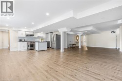 Open-concept living area featuring wood-finish flooring, recessed lighting, and a full kitchen with stainless steel appliances - 