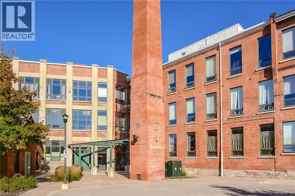Brick building exterior featuring multiple levels, expansive windows, a prominent brick chimney structure, and a covered main entrance - 26 Ontario Street Unit# 127, Guelph, ON - Outdoor
