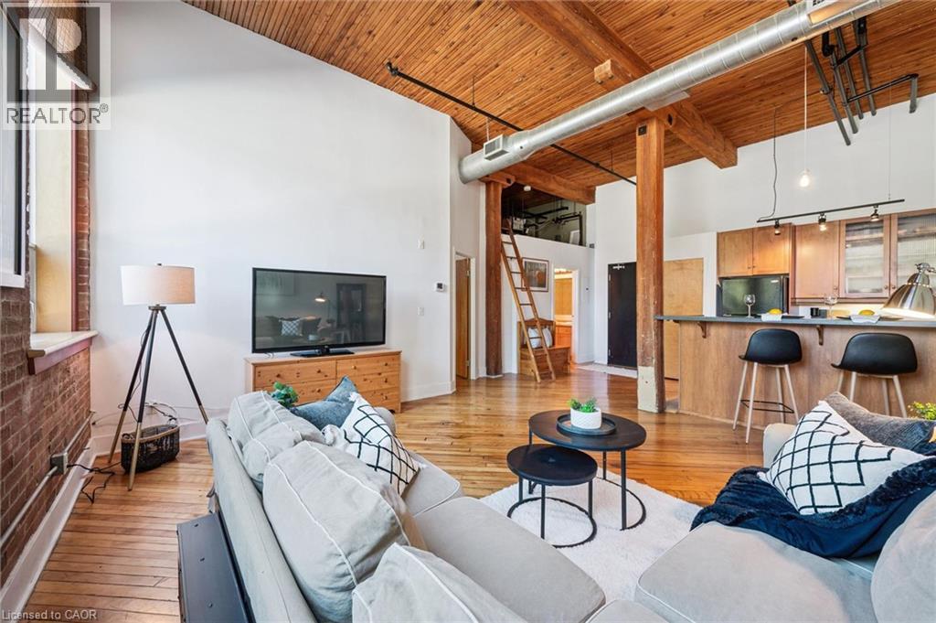 Spacious living area featuring high vaulted ceilings with exposed wood beams, wood-finish flooring, and a brick accent wall - 26 Ontario Street Unit# 127, Guelph, ON - Indoor Photo Showing Living Room