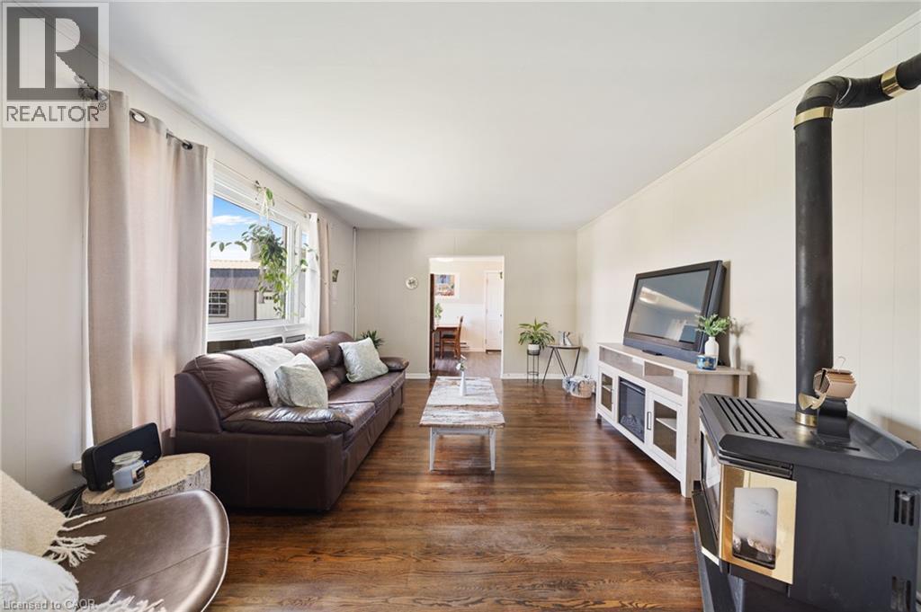 Living area featuring wood-finish flooring, a large window with white trim, and a black freestanding stove with a visible flue - 3 Bousfield Lane, Jarvis, ON - Indoor Photo Showing Living Room