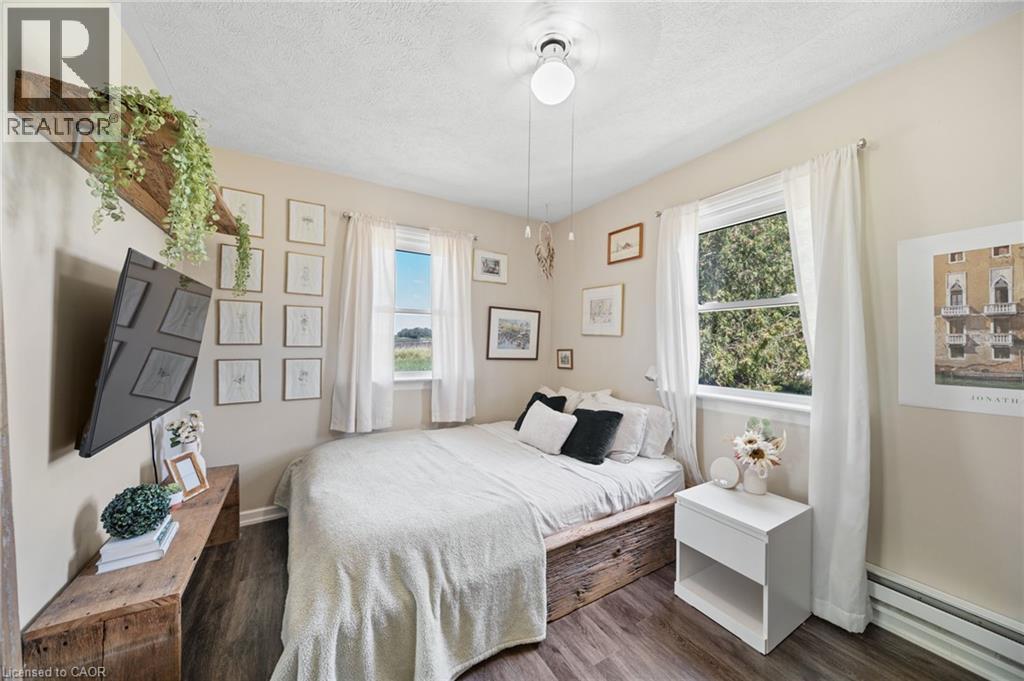 Interior room featuring wood-finish flooring, two windows with white curtains, and neutral wall tones - 3 Bousfield Lane, Jarvis, ON - Indoor Photo Showing Bedroom