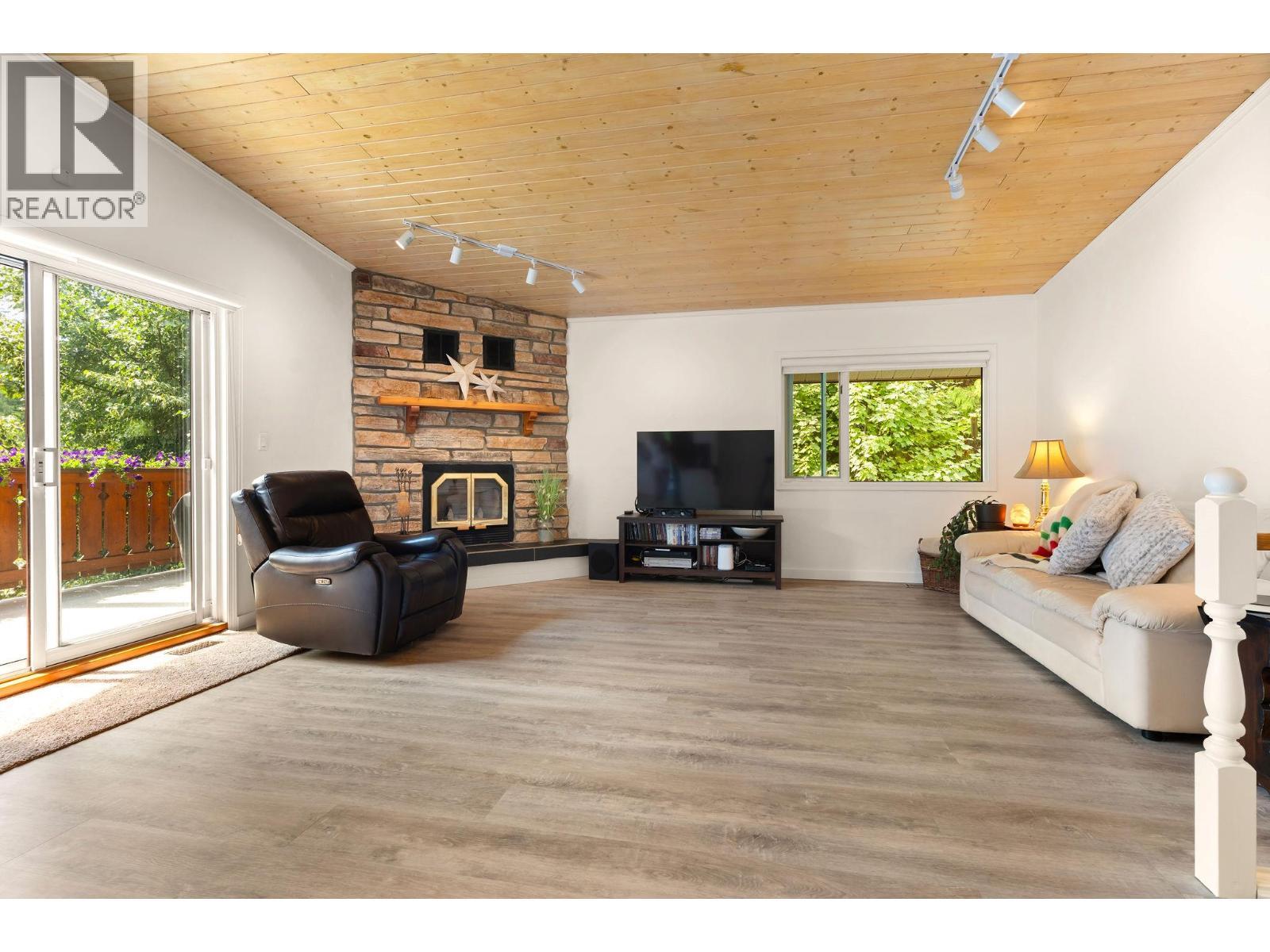 Fireplace and sliding doors to sundeck off living space - 1587 Pratico Road, Revelstoke, BC - Indoor Photo Showing Living Room With Fireplace
