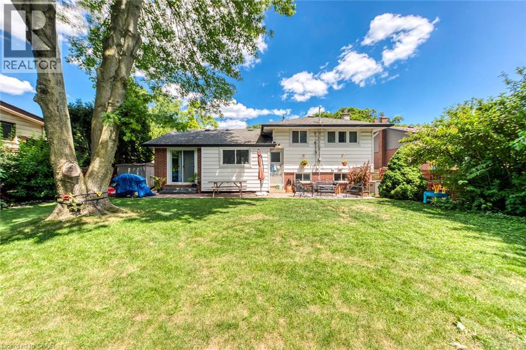 Expansive grassy backyard featuring mature trees, a patio area, and a sliding glass door entry to the home - 356 Dunlop Crescent, Burlington, ON - Outdoor