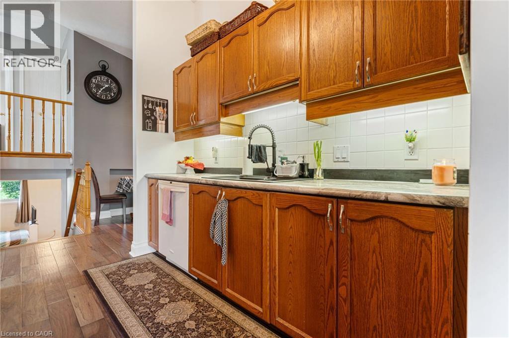 Kitchen featuring wood cabinetry, white tiled backsplash, under-cabinet lighting, and a black faucet at the sink - 2 Hampton Court, Port Dover, ON - Indoor Photo Showing Kitchen