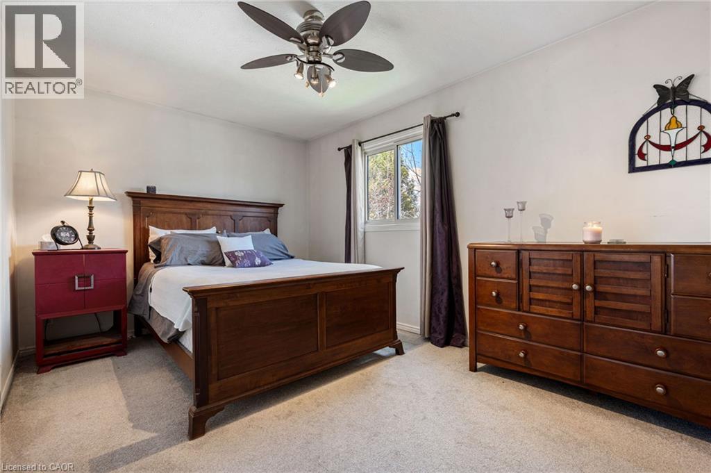Carpeted room featuring a ceiling fan with integrated lighting, a window with dark drapes, and light-colored walls - 2 Hampton Court, Port Dover, ON - Indoor Photo Showing Bedroom