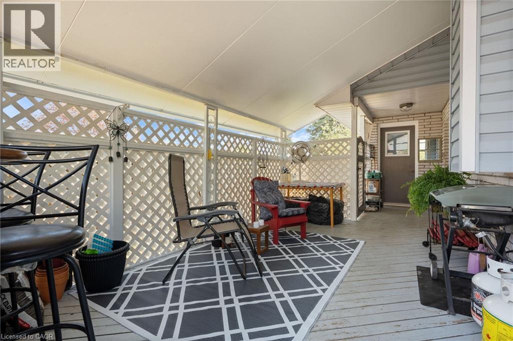 Covered patio featuring a white lattice privacy screen, light-colored wood-finish decking, and a ceiling-mounted light fixture - 2 Hampton Court, Port Dover, ON - With Deck Patio Veranda With Exterior