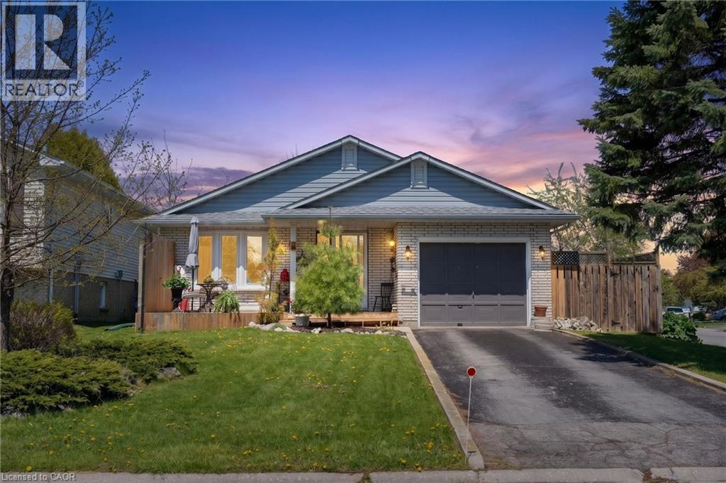 Brick and siding exterior featuring an attached garage with a dark gray door, a paved driveway, a front yard with manicured lawn and shrubs, and a raised wooden deck - 2 Hampton Court, Port Dover, ON - Outdoor