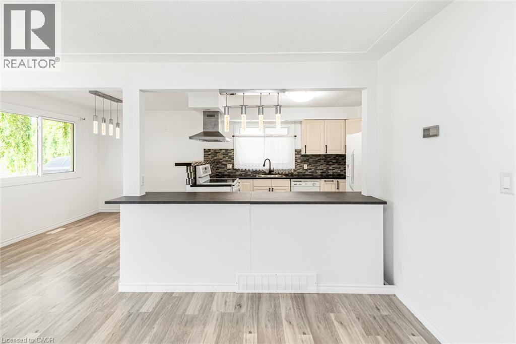 Open-concept kitchen featuring a breakfast bar with a dark countertop, white cabinetry, a stainless steel range hood, and a dark tile backsplash - 100 Mountain Avenue N, Hamilton, ON - Indoor Photo Showing Kitchen