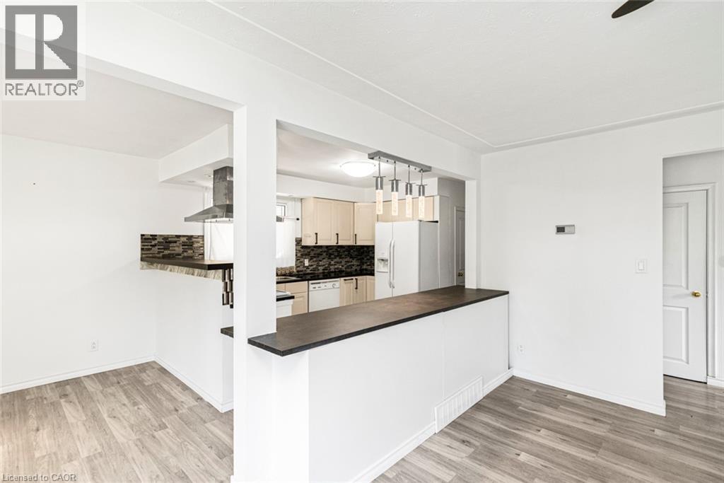 Open-concept kitchen and dining area featuring wood-finish flooring, a breakfast bar with a dark countertop, and a contemporary linear pendant light fixture - 100 Mountain Avenue N, Hamilton, ON - Indoor Photo Showing Other Room