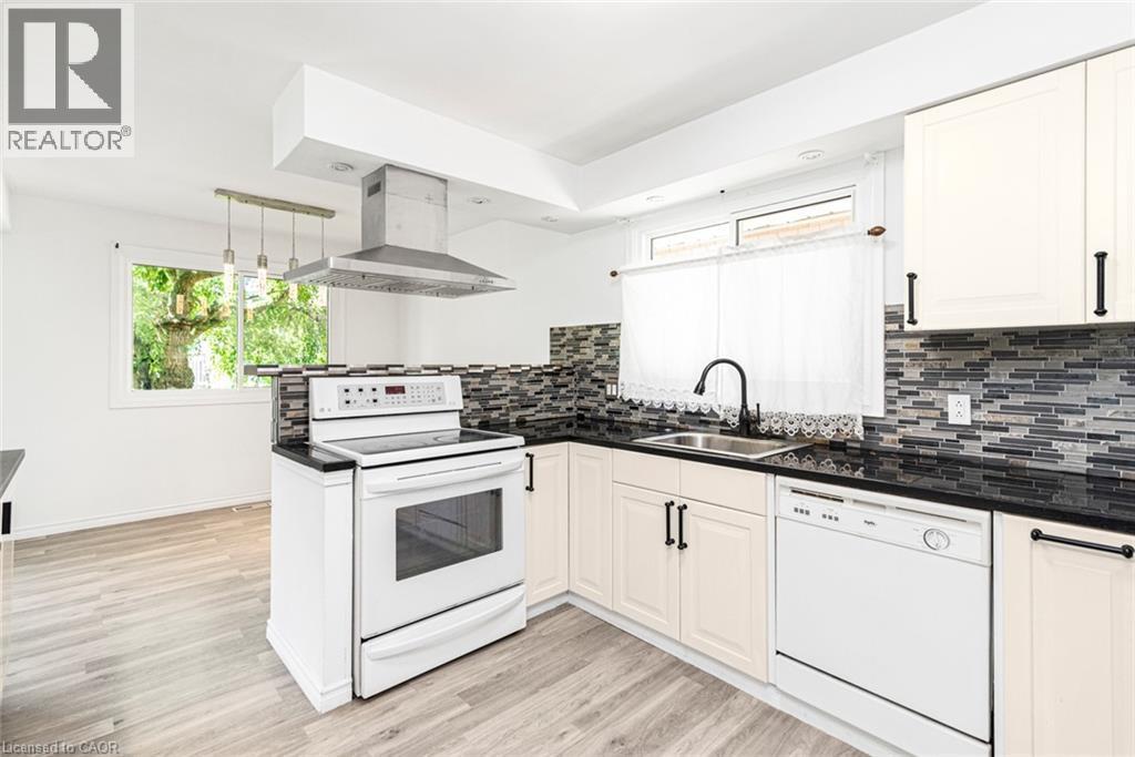 Kitchen featuring light-tone wood-finish flooring, white appliances, dark countertops, and a mosaic tile backsplash - 100 Mountain Avenue N, Hamilton, ON - Indoor Photo Showing Kitchen