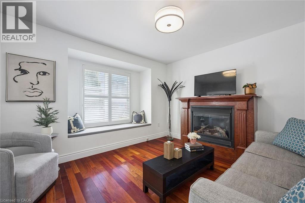 Living space featuring rich wood-finish flooring, a built-in window seat with plantation shutters, a fireplace with a wood mantel, and a flush mount ceiling light fixture - 5147 Ravine Crescent, Burlington, ON - Indoor Photo Showing Living Room With Fireplace