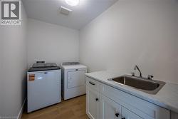 Utility room featuring wood-finish flooring, white cabinetry with dark hardware, and a stainless steel sink with a chrome faucet -