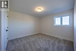 Room with neutral wall paint, gray patterned carpeting, a white interior door with black hardware, and a window with white trim -