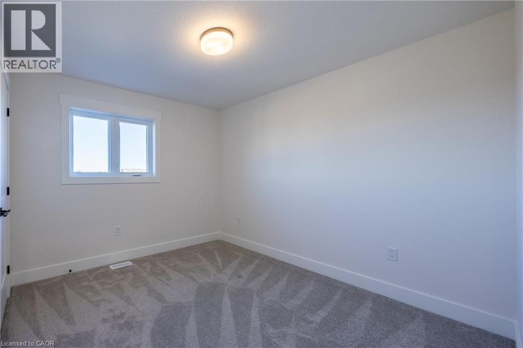 White-painted interior room featuring a window with white trim, a flush-mount ceiling light, and gray patterned carpeting - 111 Amber Street, Waterford, ON - Indoor Photo Showing Other Room