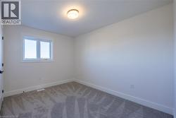 White-painted interior room featuring a window with white trim, a flush-mount ceiling light, and gray patterned carpeting -