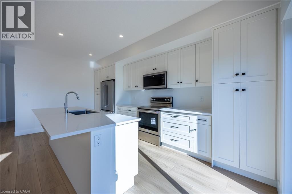 Modern kitchen featuring white cabinetry, stainless steel appliances, a center island with an undermount sink, recessed lighting, and wood-finish flooring - 111 Amber Street, Waterford, ON - Indoor Photo Showing Kitchen