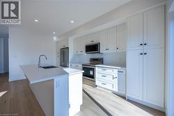 Modern kitchen featuring white cabinetry, stainless steel appliances, a center island with an undermount sink, recessed lighting, and wood-finish flooring -