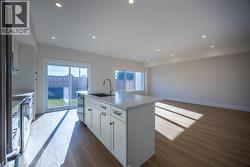 Expansive kitchen and living area featuring a central island with integrated sink, stainless steel appliances, wood-finish flooring, recessed lighting, and a sliding glass door opening to the backyard -