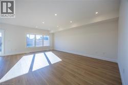 Spacious room featuring wood-finish flooring, recessed lighting, expansive windows, white baseboards, and a sliding glass door -