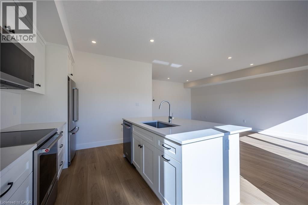 Modern kitchen featuring white shaker cabinetry, stainless steel appliances, a center island with sink and integrated dishwasher, and wood-finish flooring - 115 Amber Street, Waterford, ON - Indoor Photo Showing Kitchen With Upgraded Kitchen