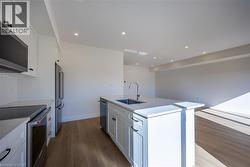 Modern kitchen featuring white shaker cabinetry, stainless steel appliances, a center island with sink and integrated dishwasher, and wood-finish flooring -