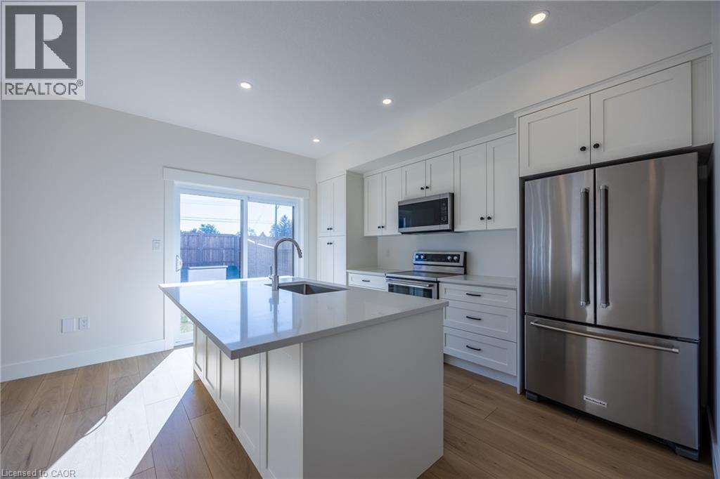 Modern kitchen featuring a central island with an undermount sink, stainless steel appliances, white cabinetry, recessed lighting, and wood-finish flooring - 115 Amber Street, Waterford, ON - Indoor Photo Showing Kitchen