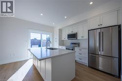 Modern kitchen featuring a central island with an undermount sink, stainless steel appliances, white cabinetry, recessed lighting, and wood-finish flooring -