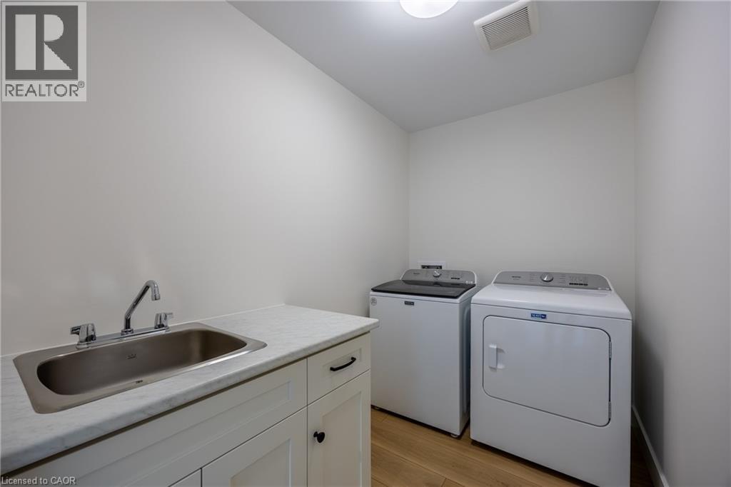 Laundry room with wood-finish flooring, white cabinetry, integrated stainless steel sink, and light-colored countertop - 115 Amber Street, Waterford, ON - Indoor Photo Showing Laundry Room