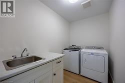 Laundry room with wood-finish flooring, white cabinetry, integrated stainless steel sink, and light-colored countertop -