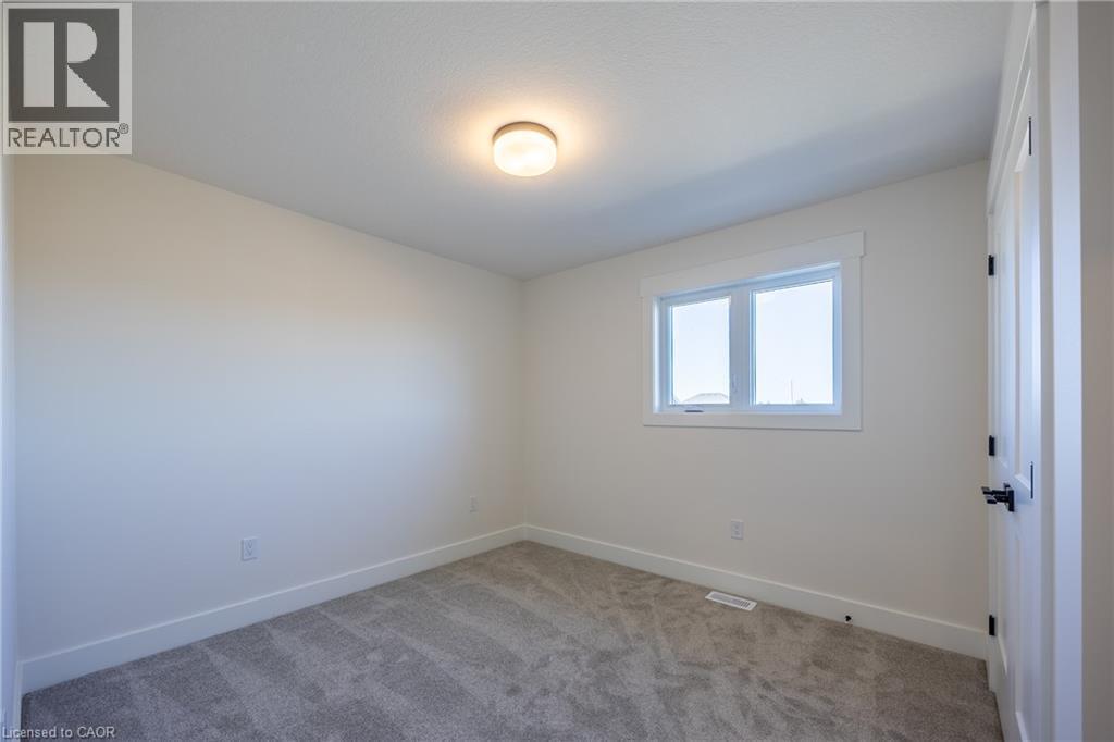 Bright room with a neutral color palette, featuring a double-paned window, soft gray carpet, white baseboards, and a flush-mount ceiling light fixture - 115 Amber Street, Waterford, ON - Indoor Photo Showing Other Room