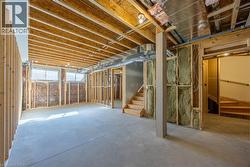 Unfinished basement featuring concrete flooring, exposed wooden joists, framed walls, and two visible wooden staircases -