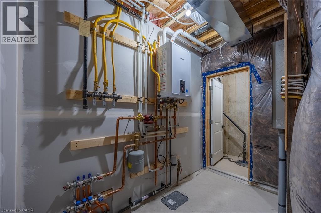 Utility area featuring a wall-mounted tankless water heater, exposed copper and yellow gas lines, visible electrical conduits, unfinished drywall, and a concrete floor - 115 Amber Street, Waterford, ON - Indoor Photo Showing Basement